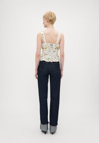 Blomsterprydd, ärmlös peplum-top med en figurnära bodice; kombinerad med mörka denimbyxor med uppvikta nederdelar och spetsiga klackar.