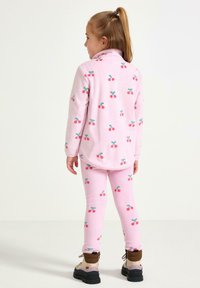 Lyserødt fleece sæt med kirsebærmotiver; top med høj krave og leggings med elastisk talje; parret med brune støvler.