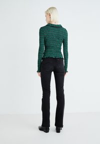 Top de manga larga de patrón verde con un diseño ajustado y un dobladillo con volantes, combinado con jeans negros ajustados y botines negros. 