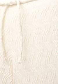 Tissu blanc texturé avec des motifs ondulés, doté d'une taille nouée. Le matériau semble léger avec une texture légèrement élevée.