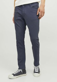 Temno modri bombažni hlače s slim fit krojem, z značilnim pet-pocket dizajnom in gladko teksturo, kombinirane z črnimi visokimi športnimi copati.