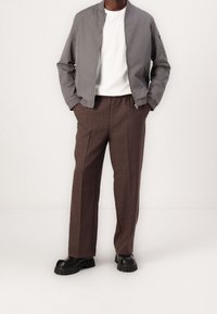 Šedá bombardovací bunda, bílý tričko, hnědé kostkované kalhoty a černé robustní boty. Hladká látka, uvolněný střih, elastický pas na kalhotách.