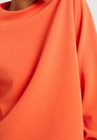 Oranges Sweatshirt aus weichem, glattem Stoff mit lockerer Passform. Verfügt über einen weiten Boot-Ausschnitt und drapierte Ärmel.
