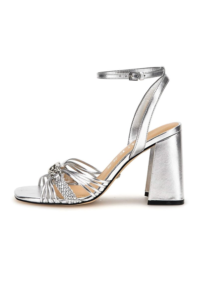 Sandal con tacco a blocco largo in metallo argento, dotata di cinturino alla caviglia e dettagli intrecciati sulla punta. Texture liscia e design aperto.