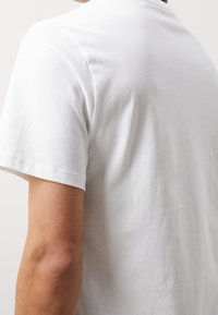 Hvid bomulds t-shirt set bagfra, med en klassisk pasform, korte ærmer og en glat tekstur. Ingen bemærkelsesværdige designelementer synlige.