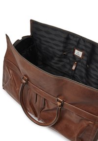 Sac de voyage en cuir marron avec un dessus zippé, des poches avant et des doubles poignées. L'intérieur présente une doublure à motifs noirs et une étiquette.