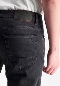 Mustad džinsid mustast denimist, millel on tekstuuriga must nahkplekk logoga, tagakoti detail ja sirge lõikega disain.