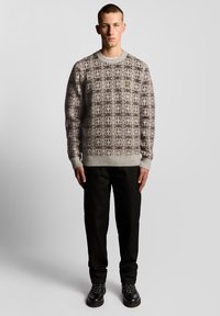 Πουλόβερ με γκρι πλεκτό σχέδιο, με ριμπ λαιμόκοψη και μανσέτες, συνδυασμένο με μαύρο παντελόνι ίσιας γραμμής και μαύρες δερμάτινες μπότες με κορδόνια.