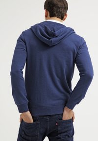 Sudadera azul con capucha, puños y dobladillo de canalé; fabricada en un tejido suave; presenta un diseño liso sin patrones ni acentos.