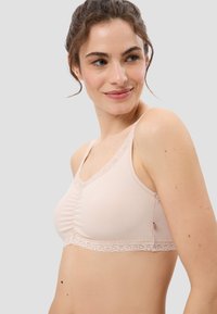 Heller rosaner BH aus weichem Material mit gerippter Textur. Hat eine Spitze entlang des Ausschnitts und des unteren Randes, mit einem gerafften Zentrum.