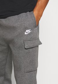 Grå cargo sweatpants gjorda av mjukt tyg, med sidofickor och en vit Nike-logotyp på vänstra låret.