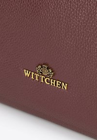Ciemnoczerwona torebka skórzana o fakturze z złotym tłoczonym logo "Wittchen" oraz dekoracyjnym detalem w kształcie herbu.