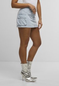 Hellblauer Denim-Minirock mit zwei Seitentaschen, kombiniert mit silberfarbener, metallic glänzender Stiefelette mit spitzer Zehenform und hohen Absätzen.