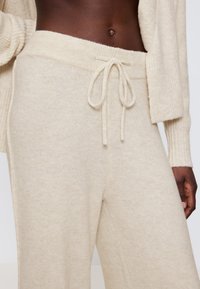 Beige Strick-Loungewear-Hosen mit einem Kordelzugbund. Der weiche, strukturierte Stoff bietet eine lockere Passform und weite Beine.