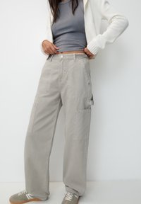 Pantaloni cargo grigi chiari a gamba larga con più tasche, realizzati in cotone. Il tessuto ha una consistenza liscia e una vestibilità comoda.