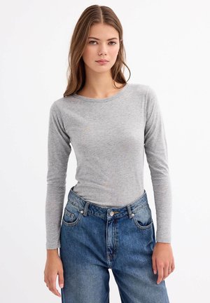 Top gris de manga larga hecho de tela suave, combinado con vaqueros de denim azul de cintura alta que presentan detalles de botones y bolsillos.