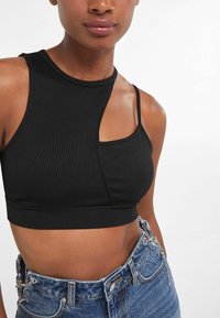 Svart ribbat crop-top med asymmetrisk design, med hög halsringning och en axelrem. Matchas med högmidjade denimshorts.