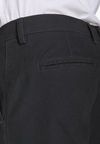 Pantaloni neri intrecciati con una texture liscia, caratterizzati da una vestibilità slim e un sottile motivo a righe. Includono una tasca posteriore con design a welt.