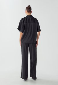 Set composto da camicia in raso nero e pantaloni a gamba larga, con maniche corte, vestibilità ampia e texture liscia. L'outfit presenta un design minimalista.