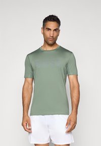 T-shirt de sport vert à manches courtes en tissu lisse, avec un logo "BOSS" subtil sur la poitrine, associé à un short blanc.