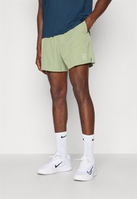Svijetlozeleni kupaći šorts s bočnom džepom i bijelim logom, uparen s bijelim Nike tenisicama i čarapama do članaka s crnim logom.