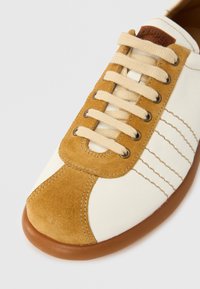 Vit och beige mockasneaker med beige snören, brun sula och sydda detaljer på tå- och sidpanelen.