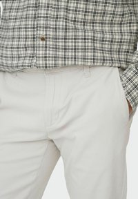 Chemise à carreaux en tissu noir et blanc, dotée d'une fermeture à boutons. Pantalon beige, slim-fit avec poches, texture lisse.