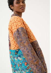 Jachetă patchwork din țesături portocalii, albastre și maronii cu modele intricate. Mâneci lungi și o croială lejeră, evidențiind texturi variate.