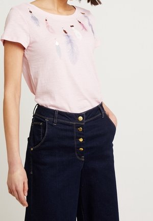 Lichtroze T-shirt met korte mouwen en veermotieven in pasteltinten, gecombineerd met donkerblauwe, hooggetailleerde jeans met gouden knoopaccenten.