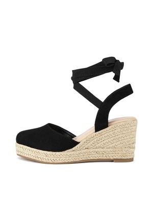 Čierne semišové sandále na platforme s pleteným juta podpätkom a čiernymi látkovými remienkami, ktoré sa prekrížia okolo členka. Zaoblený tvar špičky a hladký povrch.
