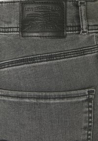 Zwart leren label op grijze spijkerbroek, met textuurstiksel en een zichtbaar zakontwerp met een lichte glans.