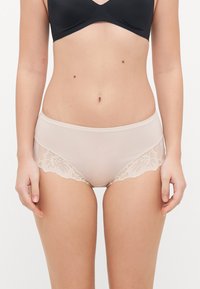 Beige hipster panties with a smooth fabric front and delicate lace trim along the sides. Soft texture, low-rise design, and scalloped edges.