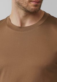 Bruine katoenen t-shirt met een zachte textuur, ronde halslijn en korte mouwen, weergegeven van borsthoogte naar boven. Glad en aansluitend ontwerp.