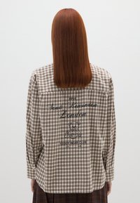 Camicia a quadri marrone e crema con maniche lunghe, dotata di yoke sulle spalle, scritta "South Kensington London" sul retro e una grafica di un orsacchiotto.
