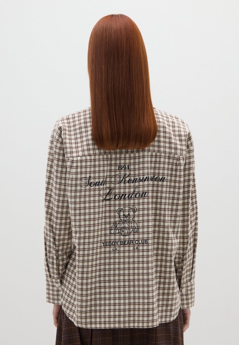 Camicia a quadri marrone e crema con maniche lunghe, dotata di yoke sulle spalle, scritta "South Kensington London" sul retro e una grafica di un orsacchiotto.