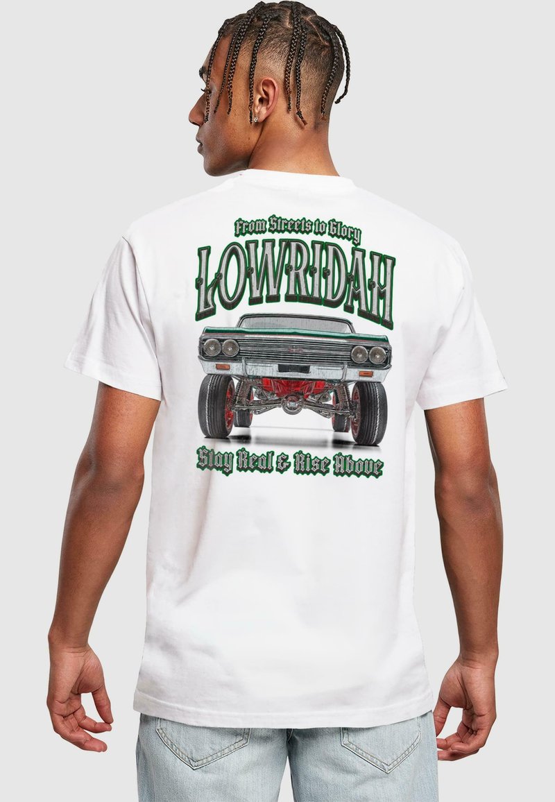 T-shirt blanche avec une impression graphique d'une voiture lowrider, texte vert et noir "LOWRIDAH," avec des accents rouges sur les roues.
