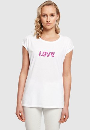 Hvit bomulls T-skjorte med rullet ermer, med rosa tekst "LOVE" i et lekent skrifttype, prydet med små blomster mønstre.