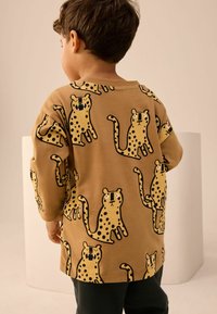 Brązowy sweter w czarne cętki, o luźnym kroju i długich rękawach. Materiał wydaje się miękki o gładkiej fakturze.