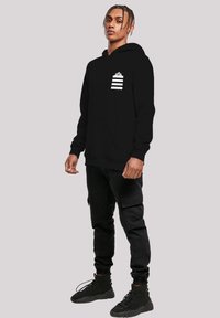 Black hoodie with a front pocket, featuring a white graphic of horizontal stripes and a crown on the left chest. Material appears soft.