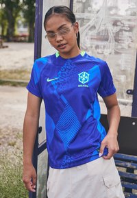 Blue athletic jersey featuring geometric patterns in varying shades, with a logo and neon green accents. Short sleeves and lightweight fabric.