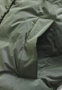 Zeleni izolirani jakni materijal s teksturiranom, naboranom površinom. Ima šivene šavove i otvoreni džep. Mekan, lagan materijal.