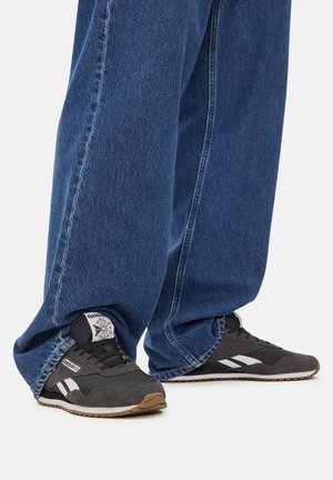 Czarne i szare buty sportowe z białymi akcentami, z teksturowaną cholewką z tkaniny i gumową podeszwą, noszone z luźnymi niebieskimi dżinsami.