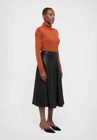 Rusk turtleneck-neule, musta nahkainen kellotettu hame ja mustat kärkitossut; sileät tekstuurit, tiukka vyötärö, polvipituinen hame.