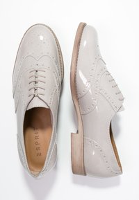 Chaussures Oxford en cuir verni beige avec des détails brogue, dotées d'un talon en bois plat et d'une forme à bout arrondi.