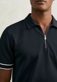 Tricou polo negru dintr-un material texturat, cu închidere prin fermoar și accente striped albe pe mâneci.
