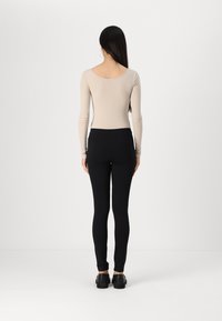 Bodysuit beige à manches longues côtelé associé à des leggings noirs. La tenue présente un dos échancré et une silhouette ajustée, avec des chaussures noires.