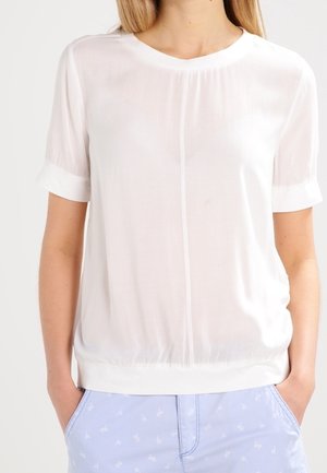 Blusa blanca de manga corta con un cuello redondo y un brillo sutil. Presenta un dobladillo fruncido y una tela suave y ligera.