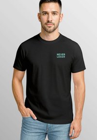 Schwarzes Baumwoll-T-Shirt mit kurzen Ärmeln, präsentiert ein türkisfarbenes "NEVER LESS®"-Logo auf der linken Brust. Enganliegend.