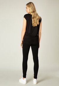 Zwart kort weggeknipt top met een losse pasvorm, geraffineerde details bij de taille, gecombineerd met zwarte leggings en witte platform sneakers.