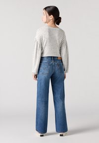 Grå og hvit stripete cropped genser med brede ermer, kombinert med høyt liv blå jeans. Jeansene har baklommer og et lærmerke.
